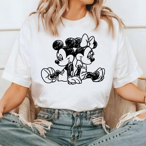 May include: White t-shirt with a black and white illustration of Mickey Mouse and Minnie Mouse holding hands.