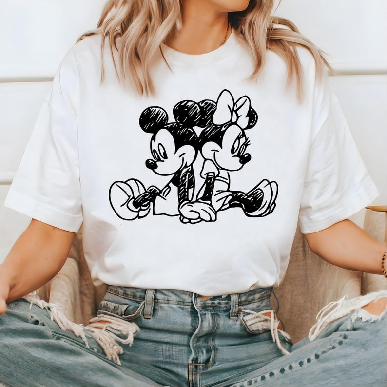 May include: White t-shirt with a black and white illustration of Mickey Mouse and Minnie Mouse holding hands.