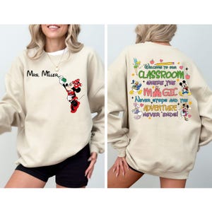 May include: Beige sweatshirt with a Mickey Mouse character design on the front and a colorful graphic with the text "Welcome to our classroom where the magic never stops and the adventure never ends!" on the back.