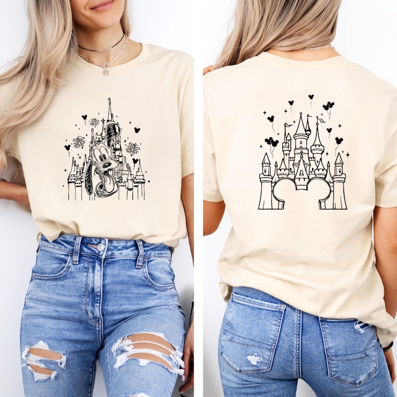 Puede incluir: Camiseta beige con una ilustraci&oacute;n en blanco y negro de un castillo y un personaje de dibujos animados. La parte trasera de la camiseta muestra un dise&ntilde;o de castillo con orejas de Mickey Mouse. La camiseta se combina con vaqueros azules.
