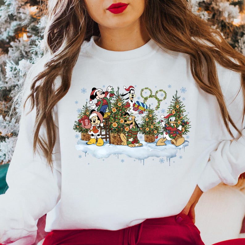 May include: White sweatshirt with a Christmas-themed design featuring Mickey Mouse, Donald Duck, Goofy, and Pluto decorating a Christmas tree. The design includes a wreath with the iconic Disney logo.