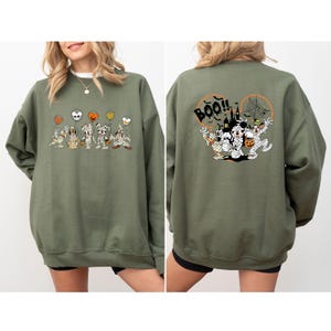 K&ouml;nnte beinhalten: Olivgr&uuml;nes Sweatshirt mit einem Halloween-Motiv. Auf der Vorderseite sind Zeichentrickfiguren als Mumien verkleidet, die Luftballons halten. Auf der R&uuml;ckseite befindet sich ein gr&ouml;&szlig;eres Design mit dem Wort "Boo!!", einem Spukhaus und weiteren Figuren.