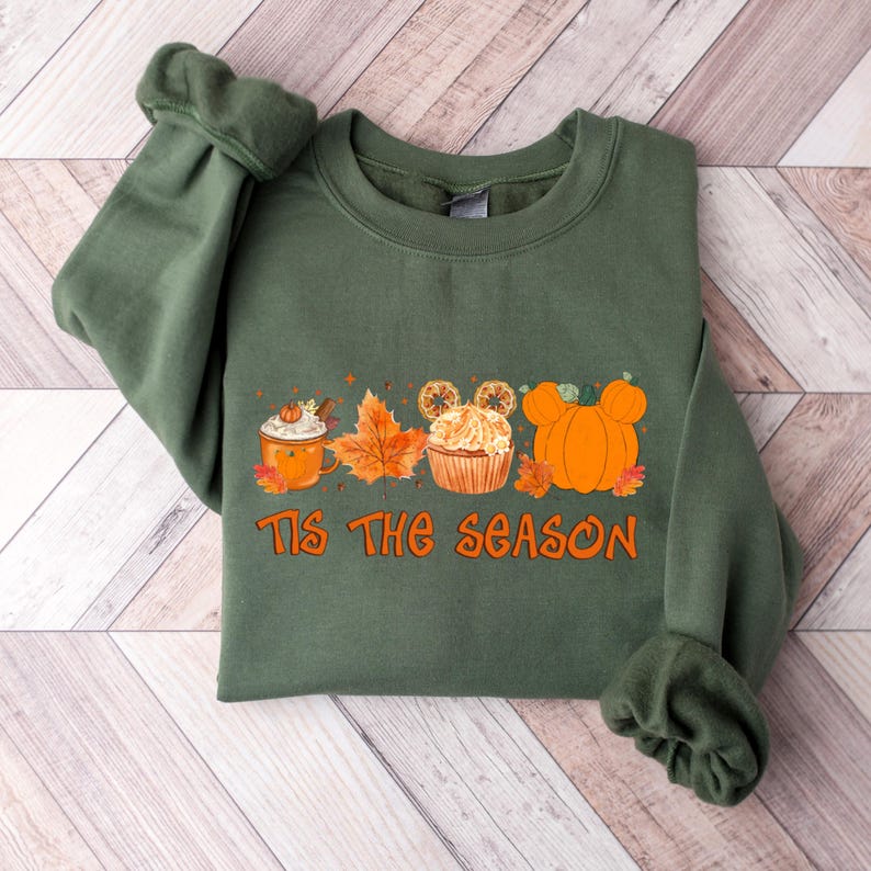 Pu&ograve; includere: Felpa verde con grafica arancione con la scritta "Tis The Season". La grafica include un latte speziato alla zucca, foglie d'autunno, un cupcake con orecchie di Topolino e zucche. Un capo a tema autunnale.