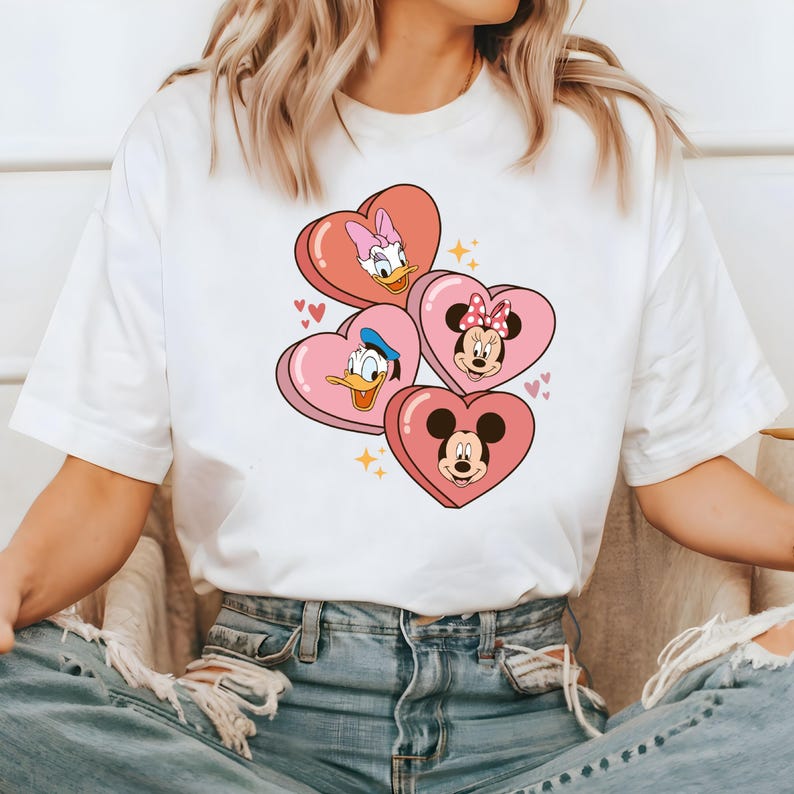 Puede incluir: Camiseta blanca con un dise&ntilde;o de coraz&oacute;n rosa con Mickey Mouse, Minnie Mouse, Donald Duck y Daisy Duck.