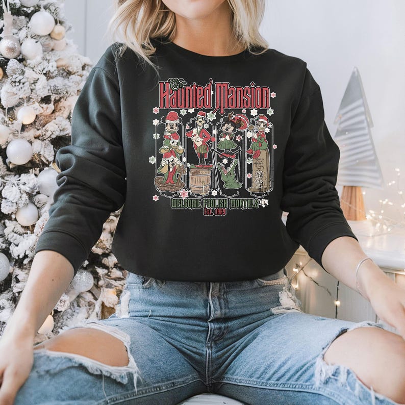 May include: Black sweatshirt with a graphic of the Haunted Mansion characters from Disney. The text "The Haunted Mansion" is printed in red and white. The text "Welcome Foolish Mortals" and "Est. 1969" are printed in white.