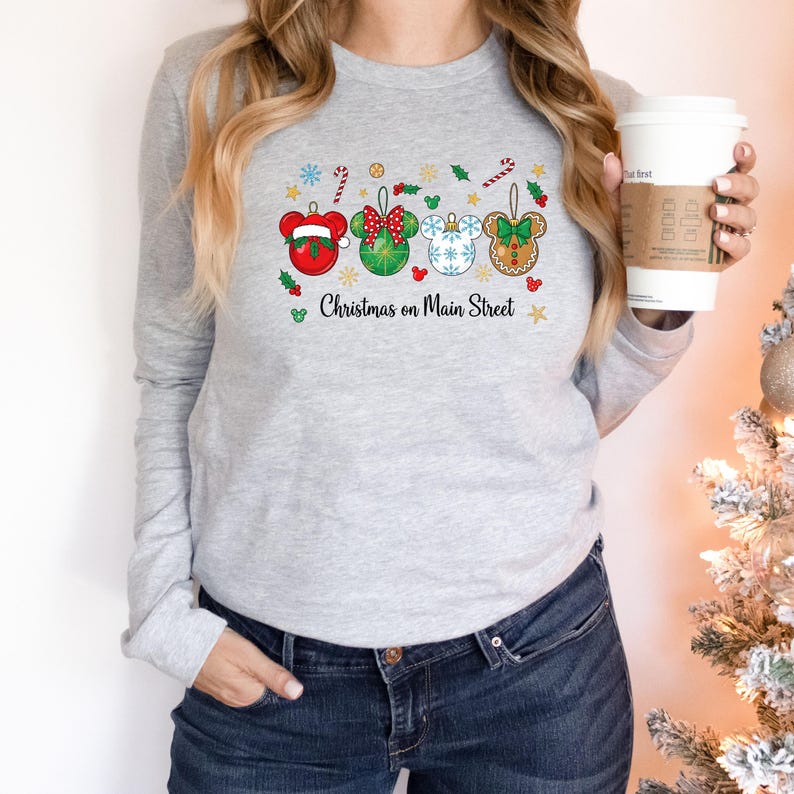 May include: A light grey long-sleeved top with a festive design. The design features four Mickey Mouse-shaped Christmas ornaments in red, green, and white, with the text "Christmas on Main Street".