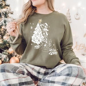 May include: A green sweatshirt with a white graphic of Mickey Mouse decorating a Christmas tree. The graphic includes a star, ornaments, and presents.