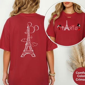 May include: Crimson red t-shirt featuring a white Eiffel Tower design with Mickey and Minnie Mouse characters. The shirt has a relaxed fit and the word "PARIS" is printed in white. The back of the shirt also features an Eiffel Tower design.
