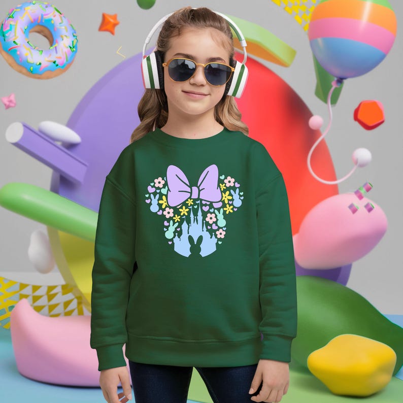 May include: A green sweatshirt featuring a Minnie Mouse-inspired design with a purple bow, flowers, bunny silhouettes, and a castle. The design is in pastel colors. The sweatshirt is worn by a person wearing sunglasses and headphones.
