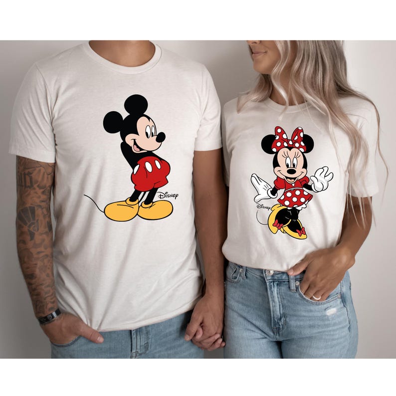 K&ouml;nnte beinhalten: Ein wei&szlig;es T-Shirt mit einem Cartoon-Bild von Mickey Mouse in roten Shorts und gelben Schuhen. Das Shirt hat den Schriftzug "Disney" aufgedruckt. Ein wei&szlig;es T-Shirt mit einem Cartoon-Bild von Minnie Mouse in einem roten, gepunkteten Kleid und roten Schuhen. Das Shirt hat den Schriftzug "Disney" aufgedruckt.