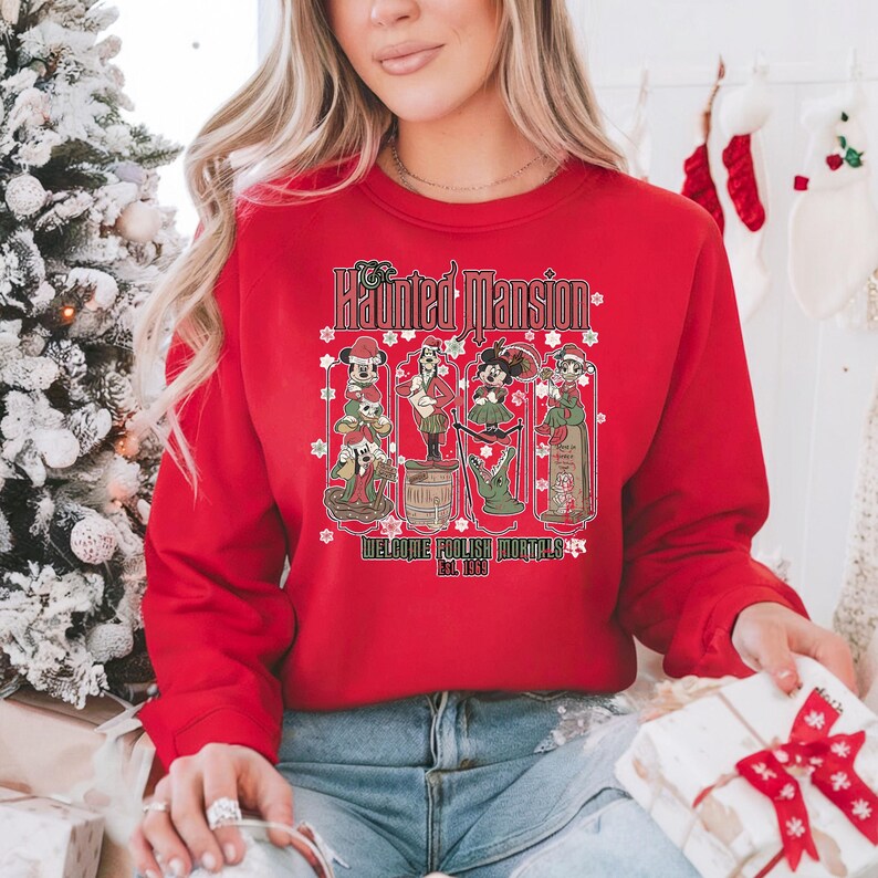 May include: Red Christmas sweatshirt with a graphic of the Haunted Mansion characters from Disney. The text on the sweatshirt reads "The Haunted Mansion Welcome Foolish Mortals Est. 1969".