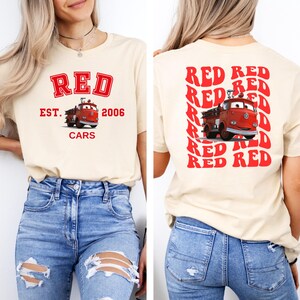 May include: A cream colored t-shirt with a red graphic of a fire truck and the text "RED EST. 2006 CARS" on the front. The back of the shirt has the word "RED" repeated in a retro style.