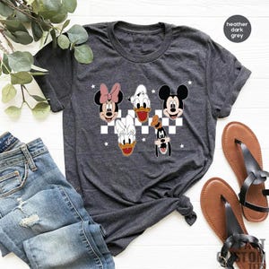 Puede incluir: Camiseta gris oscuro jaspeada con un fondo a cuadros con Mickey Mouse, Minnie Mouse, Donald Duck y Goofy.