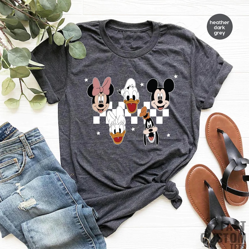 Puede incluir: Camiseta gris oscuro jaspeada con un fondo a cuadros con Mickey Mouse, Minnie Mouse, Donald Duck y Goofy.