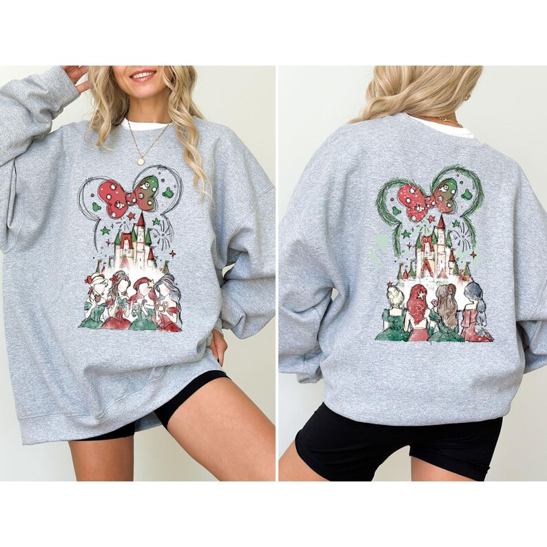 May include: A heather gray sweatshirt featuring a colorful graphic of a castle, fireworks, and several figures. The design includes a Mickey Mouse ear shape with a red bow. The sweatshirt is shown from the front and back.