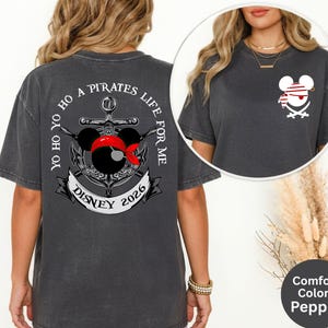 May include: Dark grey t-shirt with a pirate-themed graphic. The design features a Mickey Mouse head wearing a red bandana and a pirate hat, with an anchor and the text "Yo Ho Ho A Pirates Life For Me Disney 2026".