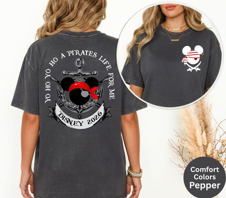 May include: Dark grey t-shirt with a pirate-themed graphic. The design features a Mickey Mouse head wearing a red bandana and a pirate hat, with an anchor and the text "Yo Ho Ho A Pirates Life For Me Disney 2026".
