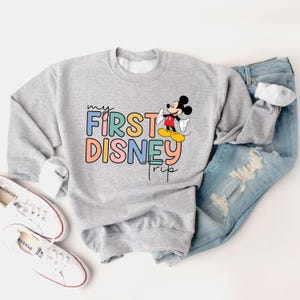 May include: A gray sweatshirt with a colorful "My First Disney Trip" graphic and a cartoon image of Mickey Mouse.