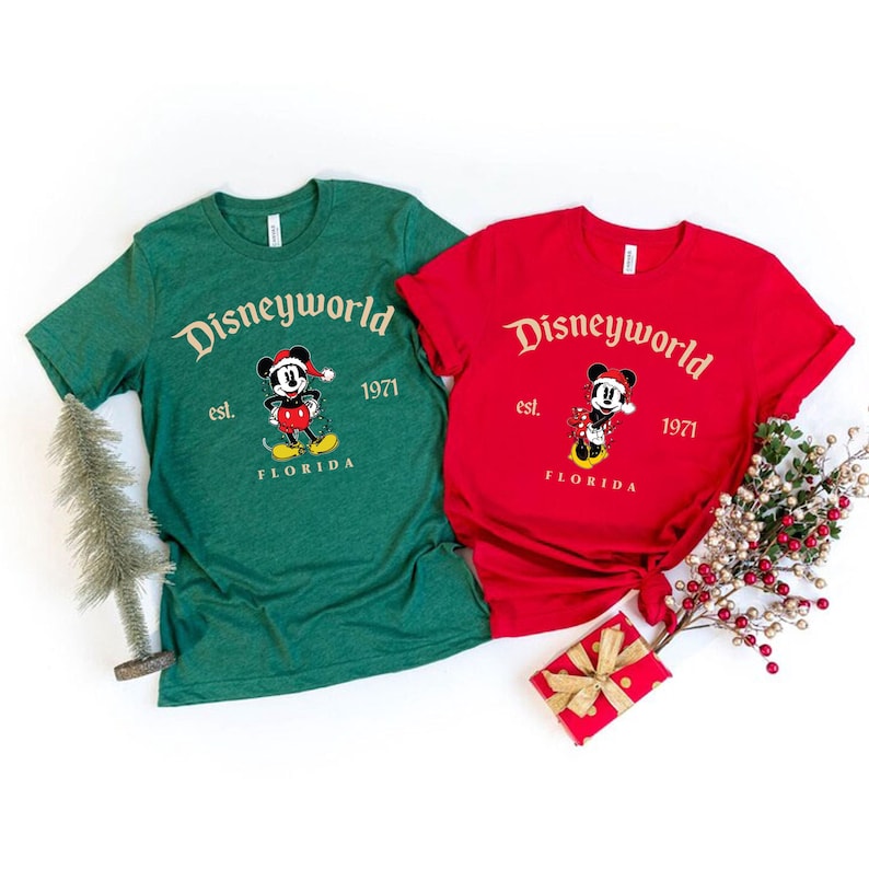 May include: Two green and red t-shirts with a Mickey Mouse wearing a Santa hat graphic. The shirts say "Disneyworld est. 1971 Florida".