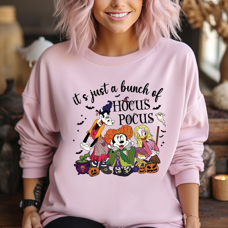 Op de afbeelding: Roze sweatshirt met een afbeelding van Mickey Mouse, Goofy en Winifred Sanderson uit Hocus Pocus. De tekst "It's just a bunch of Hocus Pocus" staat op het shirt gedrukt.