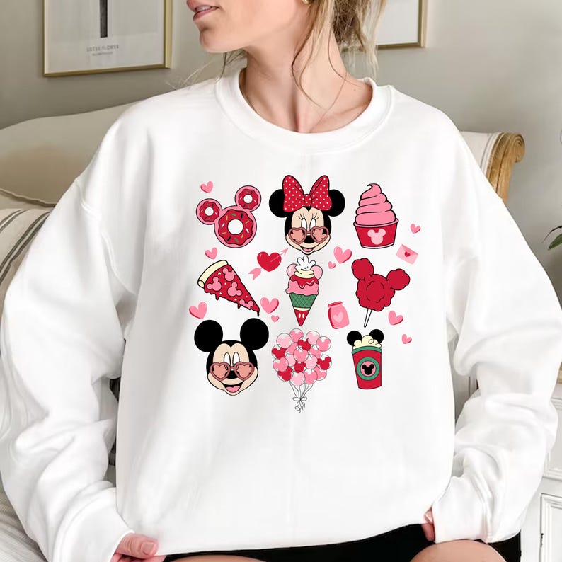 May include: White sweatshirt with a red and pink graphic print of Mickey Mouse and Minnie Mouse with hearts, donuts, ice cream, and other Valentine's Day themed items.