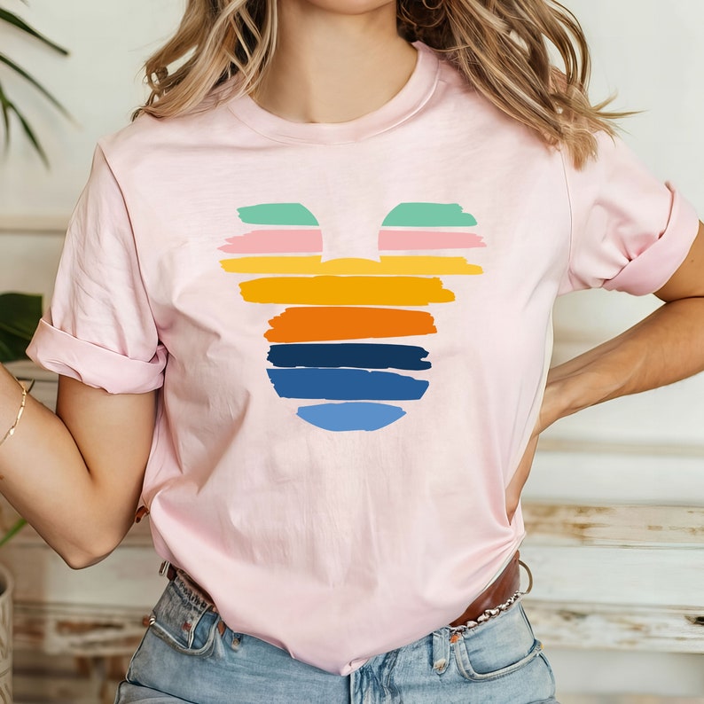 May include: A pink t-shirt with a colorful Mickey Mouse silhouette design. The silhouette is made up of horizontal stripes in shades of green, pink, yellow, orange, blue, and light blue.