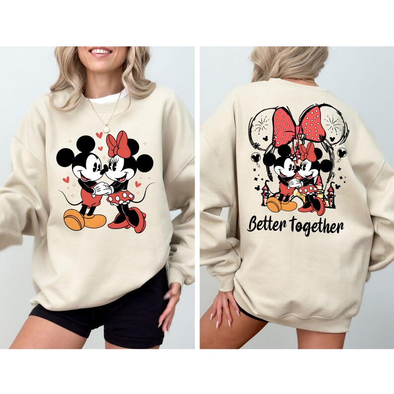 May include: A beige sweatshirt with a graphic print of Mickey Mouse and Minnie Mouse holding hands. The back of the sweatshirt has a graphic print of Mickey Mouse and Minnie Mouse with the text "Better Together".