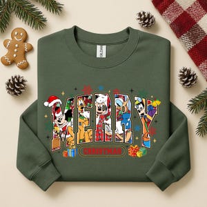 May include: A dark green sweatshirt with the word "MERRY CHRISTMAS" in a colorful, cartoon-style design. The letters are filled with images of Disney characters. Presents and snowflakes surround the text.