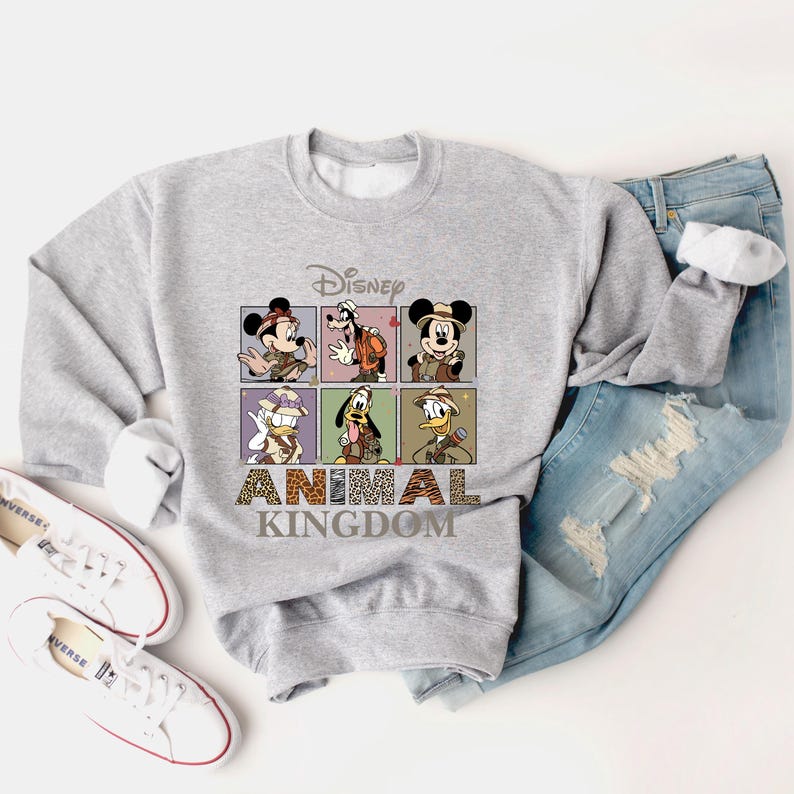 May include: A gray sweatshirt with a graphic print of Mickey Mouse, Goofy, and Donald Duck in safari outfits. The text "Disney Animal Kingdom" is printed below the characters.