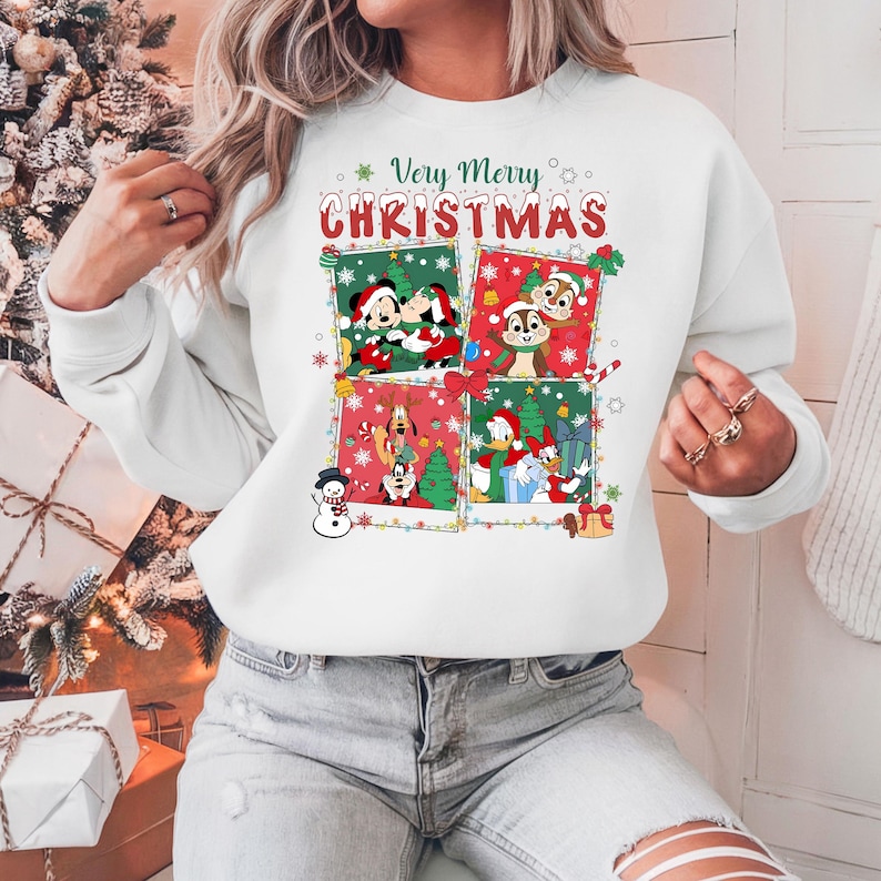 May include: White sweatshirt with a colorful graphic featuring Disney characters in Christmas scenes. The text "Very Merry Christmas" is displayed above the images. The design includes Mickey and Minnie Mouse, Chip and Dale, Goofy, Donald Duck, and more.