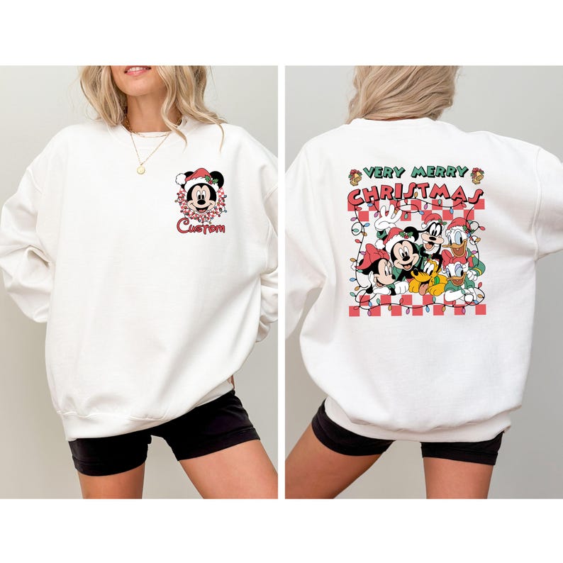May include: White sweatshirt featuring Mickey Mouse in a Santa hat with the word "Custom" below. The back of the sweatshirt displays a "Very Merry Christmas" design with Mickey, Minnie, Donald, and Goofy.