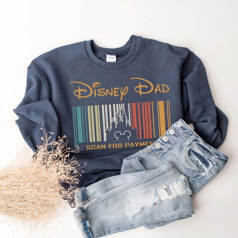 May include: A navy blue sweatshirt with the text "Disney Dad" and a vintage-style barcode with a silhouette of Cinderella's castle and Mickey Mouse. The text "Scan for Payment" is below the barcode.