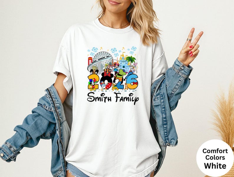 May include: White t-shirt featuring a colorful graphic with the numbers "2026" and Disney characters. The text "Smith Family" is below the graphic. The shirt has a crew neck and short sleeves.