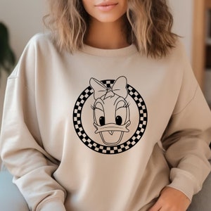 May include: A beige sweatshirt with a black and white chequered circle design featuring a cartoon duck with a bow.