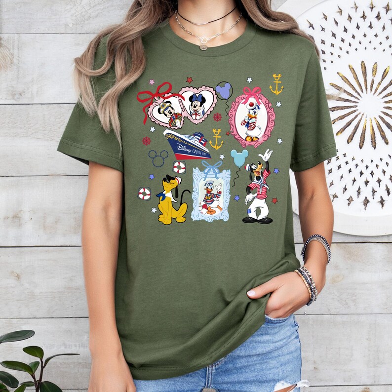 Puede incluir: Camiseta verde con un estampado colorido de personajes de Disney, incluyendo Mickey Mouse, Minnie Mouse, Donald Duck, Goofy y Pluto. El estampado presenta un crucero, anclas, estrellas y corazones. "Disney Cruise Line" est&aacute; escrito en el barco.