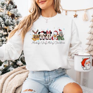Puede incluir: Sudadera blanca con un dise&ntilde;o festivo de personajes de Disney con atuendos navide&ntilde;os. El dise&ntilde;o incluye a Mickey, Minnie, Donald, Goofy y Pluto, con el texto "Mickey's Very Merry Christmas". Tambi&eacute;n se ve una taza tem&aacute;tica navide&ntilde;a.