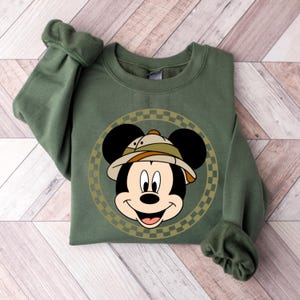 May include: A green sweatshirt with a cartoon image of Mickey Mouse wearing a safari hat. The image is surrounded by a checkered circle.