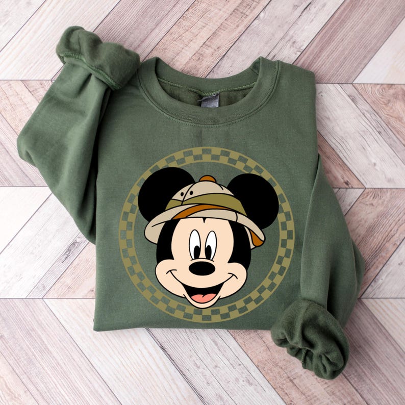 May include: A green sweatshirt with a cartoon image of Mickey Mouse wearing a safari hat. The image is surrounded by a checkered circle.