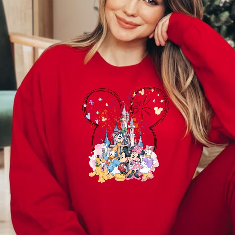 May include: Red sweatshirt with a graphic of Mickey Mouse, Minnie Mouse, Goofy, Pluto, and Donald Duck in front of Cinderella's Castle. The graphic is surrounded by a Mickey Mouse ear shape with confetti and hearts.