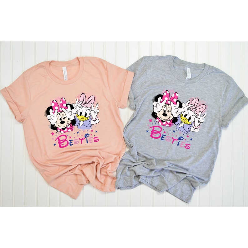 May include: Two pink and white t-shirts with a graphic of Minnie Mouse and Daisy Duck with the word "Besties" printed on them.