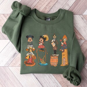 May include: Green sweatshirt featuring a vintage-style graphic print of Mickey Mouse, Minnie Mouse, Goofy, Donald Duck, and Pluto. The characters are depicted in various poses, including Mickey Mouse holding a sign that says "Ask Sand".
