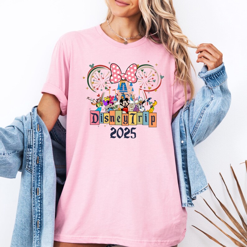 May include: Pink t-shirt with a graphic of Mickey Mouse and friends in front of Cinderella's Castle. The graphic also includes fireworks and the text "Disney Trip 2025".