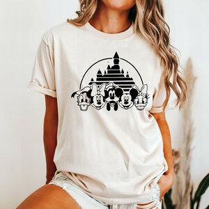 May include: A cream colored t-shirt with a black silhouette of Mickey Mouse, Minnie Mouse, Donald Duck, Goofy, and Pluto in front of a black silhouette of Cinderella's castle.