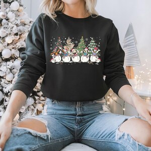 Op de afbeelding: Zwart sweatshirt met een kerstthema ontwerp met Mickey Mouse, Donald Duck, Goofy, Pluto en Minnie Mouse verkleed als sneeuwpoppen. De personages staan voor kerstbomen.