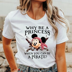 May include: White t-shirt with a graphic of a pirate Mickey Mouse with crossed swords and the text "Why be a princess when you can be a pirate?"