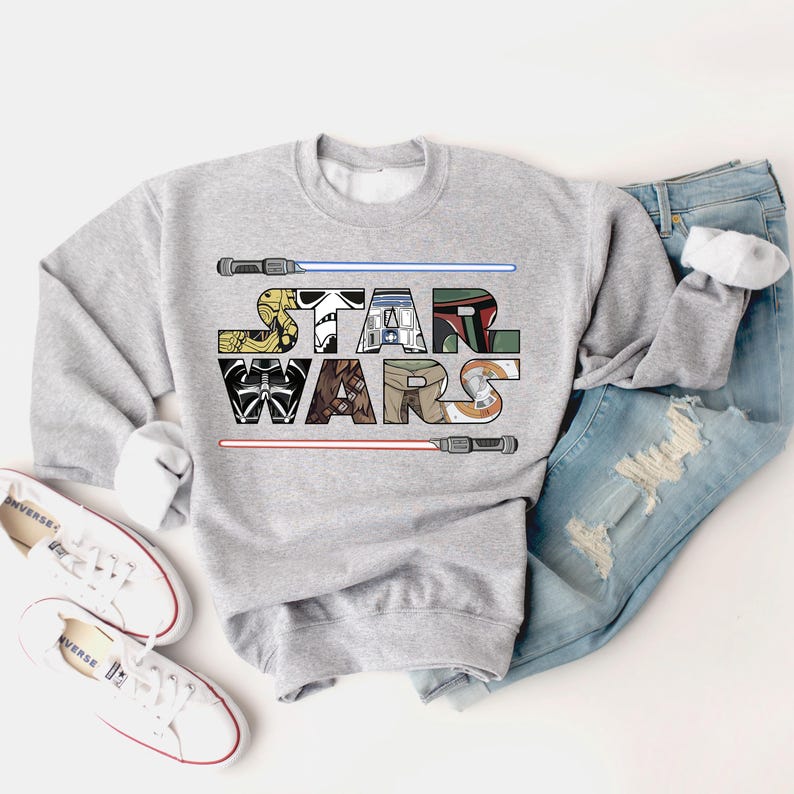 May include: A gray sweatshirt with a graphic of the Star Wars logo. The logo is made up of images of characters from the Star Wars franchise, including Darth Vader, Yoda, and R2-D2.