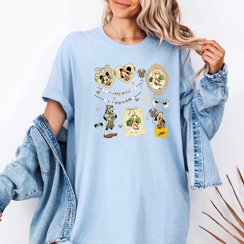 May include: Light blue t-shirt featuring various Disney character illustrations. The design includes Mickey and Minnie Mouse in heart-shaped frames, along with other characters and the text "ANIMAL KINGDOM".
