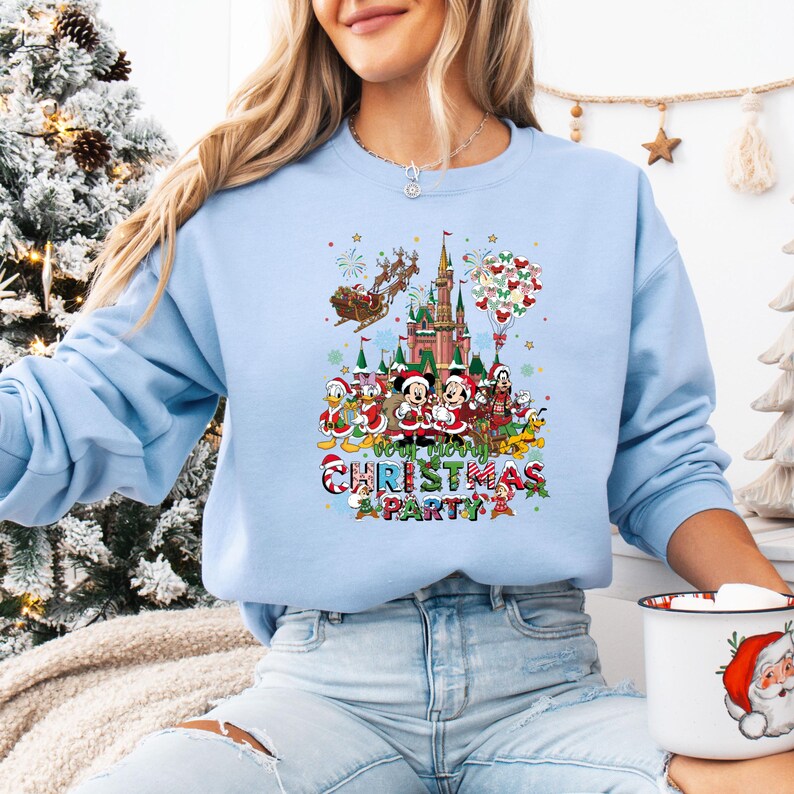 May include: Light blue sweatshirt featuring a colorful graphic of Disney characters celebrating Christmas. The design includes Mickey and Minnie Mouse, Donald Duck, and a castle, with the text "Your Merry Christmas Party".