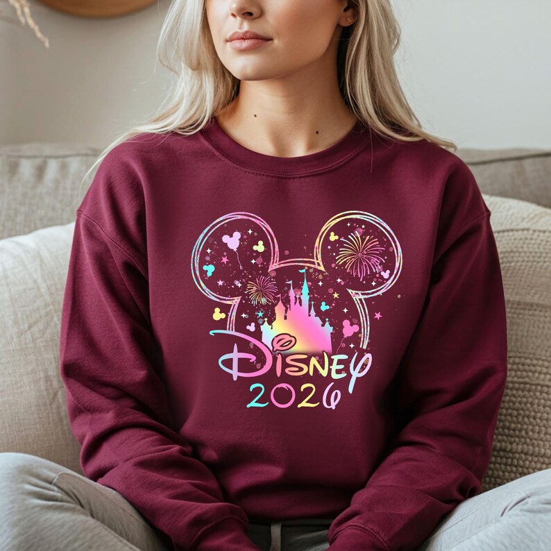 May include: Burgundy crewneck sweatshirt featuring a colorful Disney design. The design includes a castle, fireworks, and Mickey Mouse ears, with the word "Disney" and the year "2020" in a rainbow gradient.