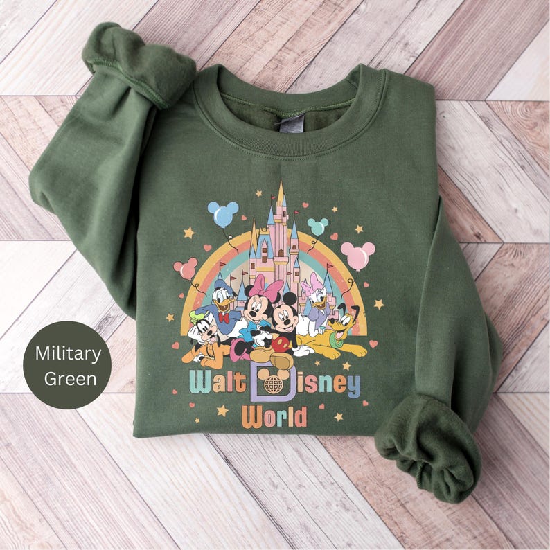 Puede incluir: Una sudadera verde con un gr&aacute;fico colorido de Mickey Mouse y sus amigos frente al Castillo de Cenicienta en Walt Disney World. El texto "Walt Disney World" est&aacute; impreso debajo del gr&aacute;fico.